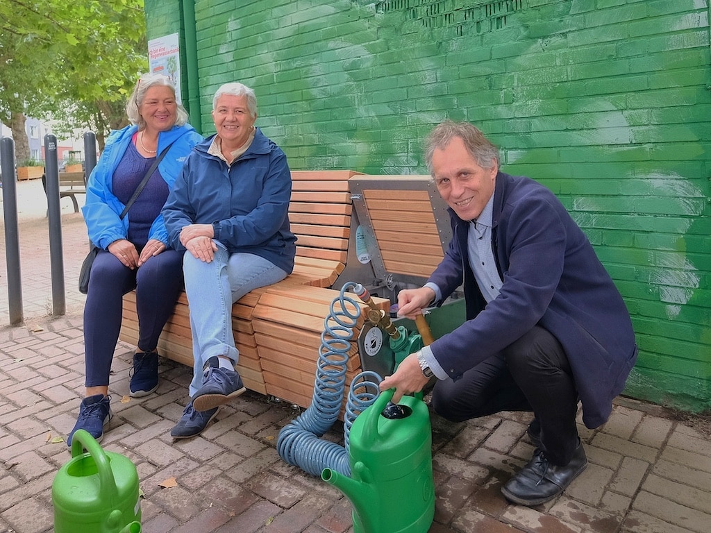 Jochen Kral (r.), Beigeordneter für Mobilität und Umwelt, zapft Wasser aus der Bank ab. Mit dem gesammelten Wasser wird ab sofort das umliegende Stadtgrün wie Staudenbeete des Hermannplatzes bewässert oder es könnten bis zu neun Bäume pro Woche mit dem kompletten Inhalt der Regenwasserbank gegossen werden. © Wilfried Meyer